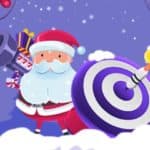 Santa holds a bazooka marked 777 and a shield with target circles drawn. A dart has hit the shield's center, and gift boxes fly in the air.